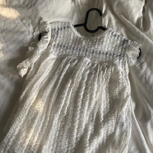 Vit spetsklänning med volangärmar - Superfin vit kortklänning i spets med volangdetaljer på ärmarna och knytning i ryggen. Klänningen har ett romantiskt mönster och är lätt transparent med söt struktur. Perfekt för sommarens alla tillfällen!