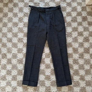  Berg & Berg kostymbyxor - Lyxiga mörkgrå kostymbyxor från Berg & Berg, tillverkade i Italien av 100% ull (kvalité). Byxorna har  pressveck, uppvikta benslut och sidfickor samt en bakficka med knapp. Hängöglan där bak är lite sliten (se bild 4) men annars är dem i fint skick. Nypris ca. 2000