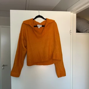Orange stickad tröja från Monki - Superfin orange stickad tröja från Monki med v-ringad krage och lite loose fit. Tröjan har långa ärmar och breda ribbade muddar vid ärmslut och nederkant. Perfekt för lager-på-lager och ger en poppig färg till din outfit.