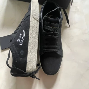 Svarta sneakers från Saint Laurent Stl 42 - Svarta sneakers från Saint Laurent med vit sula och handskriven logga på sidan. Skorna har snörning, rund tå och är tillverkade i canvas med detaljer i skinn. Klassisk och stilren design med diskreta Saint Laurent Paris-detaljer på plösen och sulan. Priset kan diskuteras vid snabb affär har du några funderingar hör av dig 🤙🏽 