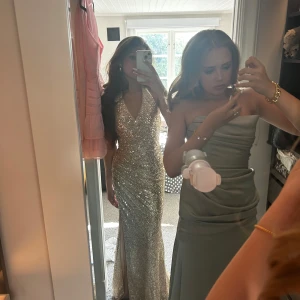 Glittrig guldig långklänning med slits - Säljer en superfin långklänning i guld med massor av paljetter. Klänningen har v-ringning, smala axelband och en snygg slits framtill. Perfekt för bal eller fest. Har använt den en gång så den är nästan helt oanvänd! Köpte den för 2890 så säljer den för 2200