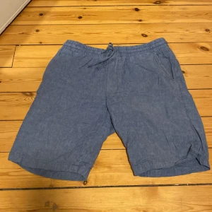 Blå linneshorts från Dressmann - Snygga blå shorts från Dressmann i linnen med avslappnad passform. De har elastisk midja med snörning och praktiska fickor både fram och bak. Perfekta för varma sommardagar när du vill vara både chill och stilren.
