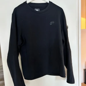 Nike tech sweatshirt storlek M - Svart långärmad tröja från Nike med diskret logga på bröstet. Enkel och stilren design med rund halsringning, perfekt för en sportig och avslappnad look. Mjuk och bekväm, passar till många outfits. Köptes för 900kr