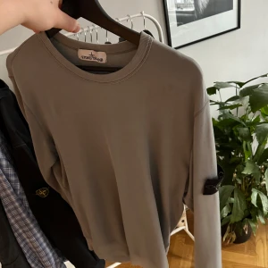 Grå tröja från Stone Island - Säljer en stilren grå tröja från Stone Island med rund hals och långärmade ärmar. Tröjan har en ikonisk logga på ärmen och är perfekt för en avslappnad look. Passar bra till både jeans och chinos.