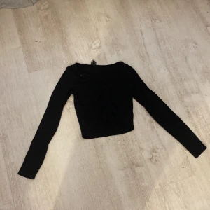 Svart ribbad topp från Monki - Säljer en svart ribbad topp från Monki i storlek XS. Toppen har långa ärmar och en snygg v-ringad design med snörning framtill. Perfekt för en stilren look!