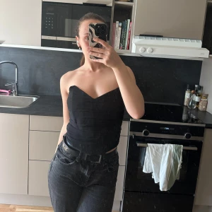 Svart axelbandslös topp - Snygg svart axelbandslös topp som passar perfekt för en kväll ute. Den har en tight passform och en stilren design som framhäver figuren. Perfekt att matcha med jeans eller kjol för en trendig look.