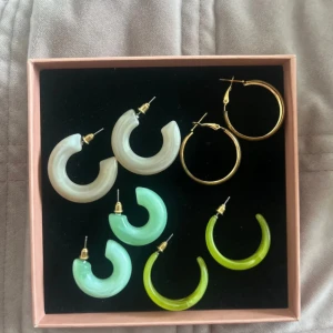 Färgglada örhängen i olika stilar - Säljer ett set med fyra par örhängen i olika färger och stilar. Inkluderar guldiga ringar samt halvgenomskinliga örhängen i ljusrosa, ljusgrönt och limegrönt. Perfekt för att mixa och matcha till olika outfits. Aldrig använda.