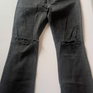 Svarta jeans med slitningar från H&M - Säljer ett par svarta jeans från H&M med coola slitningar på knäna. Jeansen har en klassisk passform och är perfekta för en avslappnad stil. De är tillverkade i ett bekvämt material som ger en skön känsla hela dagen.