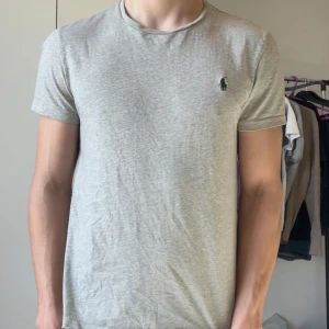 Grå t-shirt från Ralph Lauren - Säljer en stilren grå t-shirt från Ralph Lauren med korta ärmar och en liten broderad logga på bröstet. Perfekt för en avslappnad look. Passar bra till jeans eller shorts.