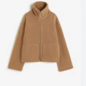 Beige teddyjacka med dragkedja - Jätte fin teddy jacka som är slutsåld och väldigt eftertraktad jackan är en mysig beige teddyjacka med dragkedja och hög krage. Jackan har två stora fickor framtill och är perfekt för kyliga dagar. Den har en avslappnad passform och är långärmad.
