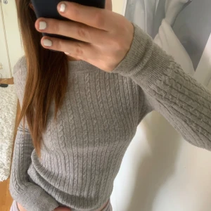 Grå stickad tröja - Säljer en stilren grå stickad tröja med kabelstickat mönster. Tröjan har långa ärmar och en bekväm passform som passar perfekt för kyligare dagar. Perfekt för en avslappnad och mysig look.