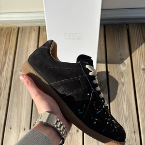 Massion Margiela - Snygga svarta sneakers med ett unikt färgglatt stänkmönster. Skorna har en rund tå och snörning framtill. Perfekta för att ge din outfit en kreativ touch.