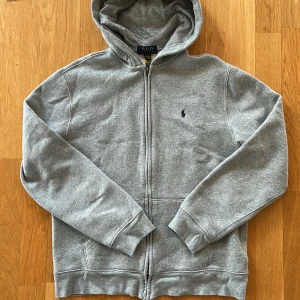 Jättesnygg äkta Ralph Lauren - Säljer en klassisk grå hoodie från Polo Ralph Lauren med dragkedja och broderad logga på bröstet. 💯Perfekt för en avslappnad stil. 👍Hoodien har långa ärmar och en bekväm passform.✅skriv till mig vid frågor och funderingar😊