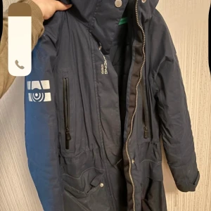 Blå parkajacka från Sail Racing - Säljer en blå parkajacka från Sail Racing i GORE-TEX-material. Jackan har dragkedja och knappar framtill samt flera praktiska fickor. Perfekt för kyliga dagar med sin långa design och skyddande huva. Mörkblå vinterjacka från sailracing - super skön och varm på vintern - den är i använt skick och är lite smutsig, ena fickan har även gått sönder men enkelt och laga (syns inte när fickan är stängd), är även missfärgat i fickan och syns lite på fickan