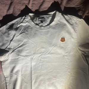 Vit äkta t-shirt från Kenzo med tigerbroderi - Säljer en stilren vit t-shirt från Kenzo med ett coolt tigerbroderi på bröstet. Perfekt för en avslappnad look. T-shirten är kortärmad och gjord i mjukt bomullsmaterial.