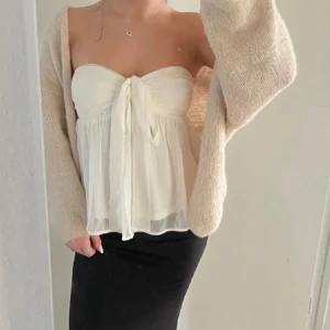 Vit axelbandslös topp med knyt du från nelly - Säljer en söt vit axelbandslös topp med knyt framtill. Toppen sitter bra vid bysten och ramlar inte ner💞