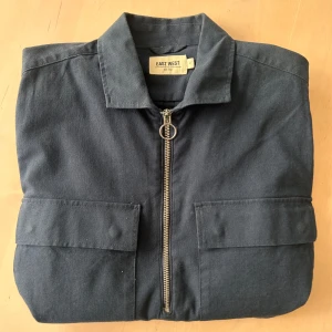 Mörkblå overshirt från East West - Säljer en mörkblå overshirt (med half-zip) från East West med dragkedja och två stora fickor framtill. Det är en extremt snygg jacka, som tyvärr blivit för liten. Har använts sparsamt. 