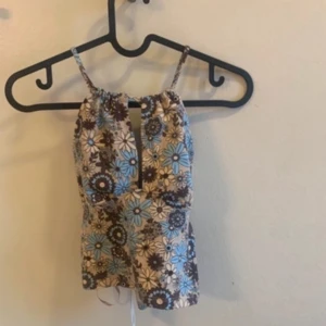 Blommig topp från Bikbok - Säljer en söt topp i brunt, blått och beige. Toppen har smala axelband. Perfekt för varma sommardagar!