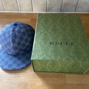 Gucci canvas blå - Säljer en stilren blå keps från Gucci med det ikoniska GG-mönstret. Kepsen har en klassisk design och är perfekt för att ge en lyxig touch till din outfit. Kommer med originalförpackning.