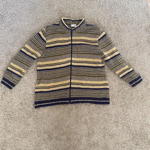 Randig stickad tröja från Bonita - Säljer en unik randig stickad tröja från Bonita i blått och beige. Tröjan har en dragkedja framtill och långa ärmar. Perfekt för kyligare dagar.