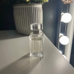 chloé parfym - Snygg parfymflaska med en elegant räfflad design och genomskinligt glas. Flaskan har en fyrkantig form och ett stilrent lock i silverfärg. Perfekt för den som vill ha en tidlös och klassisk look på sitt sminkbord.