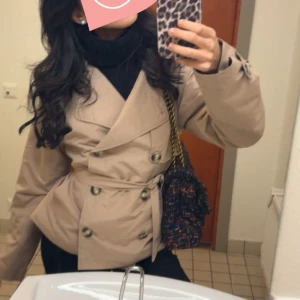 Beige trenchcoat med knappar  - Snygg beige trenchcoat med dubbelknäppning och bälte i midjan. Jackan har långa ärmar och en klassisk krage. Perfekt för höst och vår!