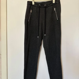 Mörkgrå mjukisbyxor från H&M - Säljer ett par mörkgrå mjukisbyxor från H&M med snörning i midjan och dragkedjor på fickorna.