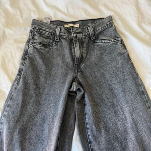 Grå baggy jeans från Levi's - Säljer ett par grå baggy jeans från Levi's med breda ben och klassisk femficksdesign. De har en hög midja och är perfekta för en avslappnad stil. Märkeslappen syns tydligt på baksidan. W25 L30
