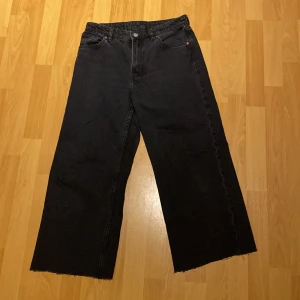Svarta vida jeans - Säljer ett par svarta jeans med en vid passform och råa kanter. Perfekta för en avslappnad stil. De har klassisk femficksdesign och knappgylf. De är klippta. 