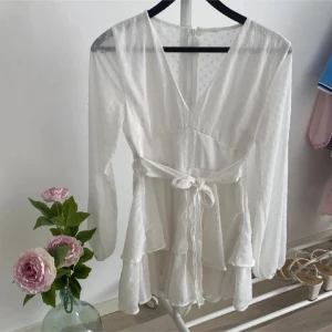 Vit omlottklänning med knytband - Säljer en elegant vit omlottklänning med v-ringning och knytband i midjan. Klänningen har även ”shorts” under vilket är sååå praktiskt!💓Är köpt för 300 och använd endast en gång!💓 priset kan diskuteras!