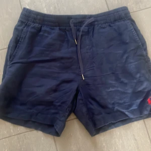 Mörkblå shorts från Polo Ralph Lauren - Snygga mörkblå shorts från Polo Ralph Lauren i linne. De har en bekväm resårmidja med snörning och två fickor bak. Perfekta för en avslappnad stil.
