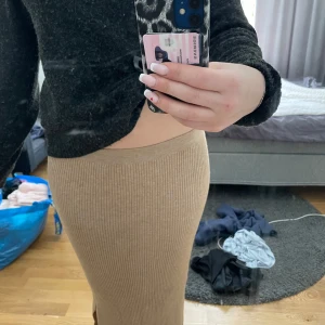 Beige ribbad kjol - Säljer en snygg beige ribbad kjol med slits. Kjolen har en tight passform och är perfekt för både vardag och fest. Den är gjord i ett mjukt och stretchigt material som formar sig fint efter kroppen.