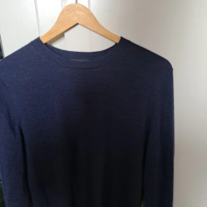 Mörkblå merinoulltröja från Dressmann - Säljer en stilren mörkblå tröja från Dressmann i mjuk merinoull. Perfekt för kyligare dagar med sin långärmade design. Tröjan har en klassisk rund hals och är ett mångsidigt tillskott till garderoben.