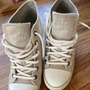 Beige sneakers med kilklack från Esprit strl 39 - Snygga beige sneakers från Esprit med kilklack och snörning. Skorna har en rund tå och är tillverkade i syntetmaterial. Perfekta för en stilren look med en twist av höjd.