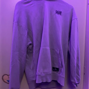 Ljus blå hoodie från stadium - Säljer en snygg lila hoodie från 'WA' broderat på bröstet. Tröjan har en klassisk känguruficka och ribbade muddar vid ärmslut och nederkant. Perfekt för en avslappnad stil! Passar för Sthlm stil
