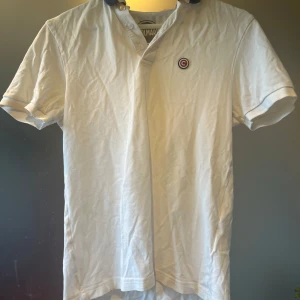 Vit pikétröja från colmar  - Säljer en stilren vit pikétröja från Colmar med en broderad logga på bröstet. Tröjan har korta ärmar och en klassisk krage i mörkblått. Perfekt för en avslappnad men ändå snygg look. Även perfekt för att ha i sommar. Storlek S. Märke Colmar. Pris kan diskuteras och skriv om ni har frågor