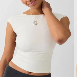 Vit ärmlös topp med öppen rygg - Snygg vit ärmlös topp med en stilren design och öppen rygg. Perfekt för en somrig look eller en utekväll. Toppen har en tight passform som framhäver figuren.