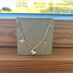 Guldhalsband med fjärilshängen - Elegant guldhalsband med små fjärilshängen. Perfekt för att lägga till en subtil touch av elegans till din outfit. Halsbandet har en tunn kedja och flera små fjärilar som hänger jämnt fördelade.