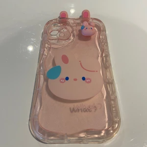 Rosa mobilskal med kaninmotiv - Sött rosa mobilskal med ett kaninmotiv och öron på toppen. Skalet är genomskinligt med en stor kaninfigur i mitten och en liten kaninfigur vid kameran. Perfekt för att ge din mobil en gullig look! iPhone 11