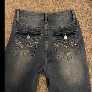 Blå jeans med broderade bakfickor - Snygga blå jeans med broderade detaljer på bakfickorna och dekorativa knappar. De har en klassisk femficksdesign och en bekväm passform.