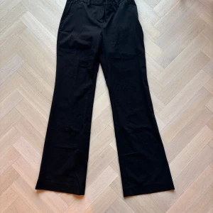 Svarta kostymbyxor från Weekday - Snygga svarta kostymbyxor från Weekday i storlek 38. Byxorna har en klassisk rak passform och är perfekta för en stilren look. De har hällor för bälte och en diskret dragkedja framtill.