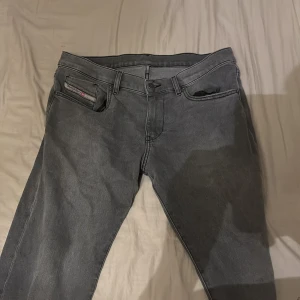 Grå jeans från Diesel - Snygga grå jeans från Diesel med klassisk femficksdesign och knappgylf. Perfekta för en avslappnad stil. Märkesdetaljer på bakfickan och etikett vid linningen.