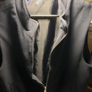 Mörkblå väst med dragkedja - Snygg mörkblå väst i skönt material. Perfekt för lager-på-lager outfits elr som lätt jacka i sommaren. Västen har en stilren design och är lätt att matcha med olika outfits. Den har innerfickor och silkes material på insidan.. Den har knappt används och är så gott som ny i sick. Passar folk runt 180cm skriv vid funderingar!