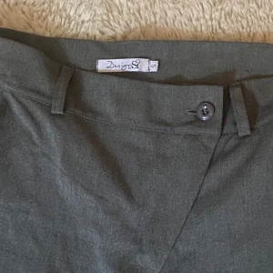 Mörkgrå kostymbyxor från Design S - Snygga mörkgrå kostymbyxor från Design S med klassisk rak passform. Byxorna har hällor för bälte, knapp och dragkedja i midjan. Perfekta för en clean och stilren look. Materialet känns mjukt och har en lätt stretch. De är även en design med unik drag kedja.