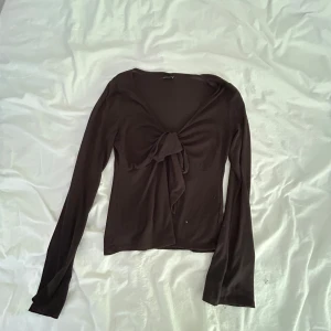 Svart omlottopp från Gina Tricot - Svart långärmad omlottopp från Gina Tricot i mjukt och stretchigt material. Toppen har en snygg knytning framtill och en djup v-ringning som ger en trendig look. Perfekt att styla med jeans eller kjol för en cool vibe.