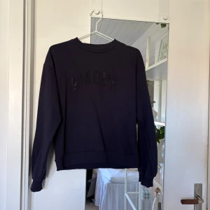 Svart sweatshirt med strass AMOUR - Svart sweatshirt med texten 'AMOUR' i svarta strasstenar på bröstet. Tröjan har rund hals, långa ärmar och ribbade muddar vid ärmslut och nederkant. Perfekt för dig som gillar en enkel men ändå snygg look. Storlek 158/164💓