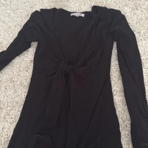 Svart långärmad klänning Design S - Svart populär topp från Design S i storlek XS/S. Toppen har en snygg knytning framtill som ger en cool touch och v-ringad hals. Passformen är normal och materialet känns mjukt och stretchigt. Mycket gott skick! Skriv för fler bilder. 