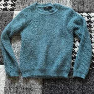Blå stickad tröja från vero moda  - Mysig blå stickad tröja  med rund hals och långa ärmar. Tröjan har en fluffig och mjuk struktur som gör den extra skön att bära. Perfekt för dig som gillar enkel och stilren design med lite extra känsla.