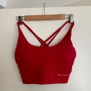 Röd träningstopp från Relode - Röd linnetopp från Relode med smala korslagda axelband i ryggen. Toppen är croppad och har en tight passform. Materialet är mjukt och stretchigt polyester som andas bra. Relode-logga tryckt framtill. Mycket sparsamt använd, nypris 449kr. 