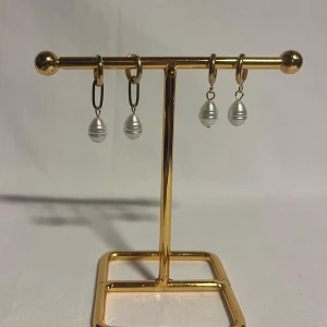 Guldörhängen med vita pärlor - Snygga örhängen med droppformade vita pärlor som hänger från guldfärgade ringar. Pärlorna har en diskret randig struktur och ger en elegant vibe. Perfekt för dig som vill ha något stilrent men ändå unikt. Passar till alla tillfällen och lyfter din look.